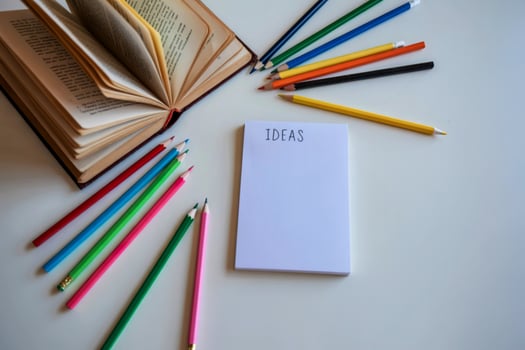 Blank notepad with colored pencils and open book photo