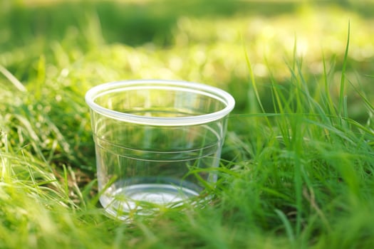 Clear plastic cup resting in lush green grass under soft sunlight photo
