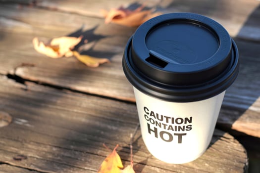 White coffee cup with black lid and caution hot text on wooden table photo