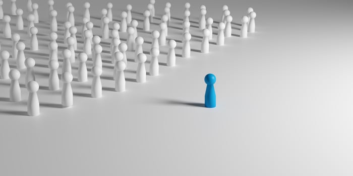 Leadership, uniqueness, individuality, and standing out from the crowd in business or social context. A single blue doll standing out from a crowd of identical white dolls. photo