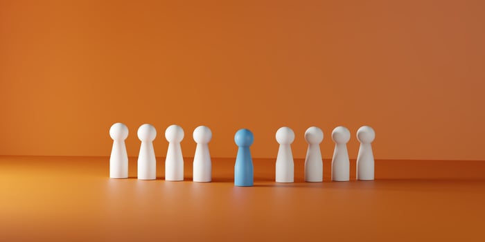 Individuality, leadership, being different, and standing out in a team or group. A single blue doll prominently positioned among a line of white dolls on a vibrant orange background. photo