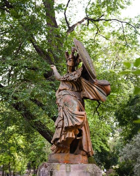 Statue of an angel with shield in park surrounded by green trees photo