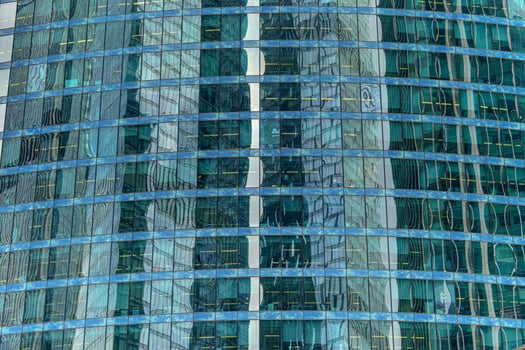 The facade of a modern building, made of green glass, reflects distorted silhouettes of nearby structures. This dynamic interplay of reflections and lines creates a visually rich urban composition. photo