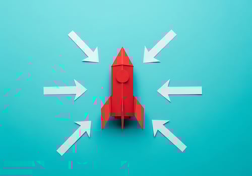 Red Paper Rocket Ship With White Arrows Pointing Towards it Centered on a Teal Background Representing Launch and Focus photo