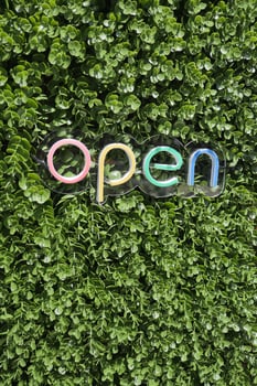Colorful open sign against green foliage backdrop photo
