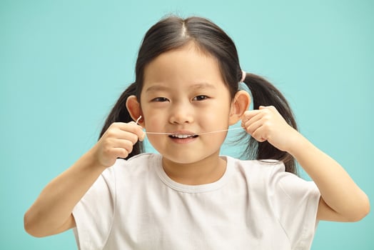 Lovely five years old chinese girl cleans herself teeth by means dental floss, headshot portrait on blue isolated. photo