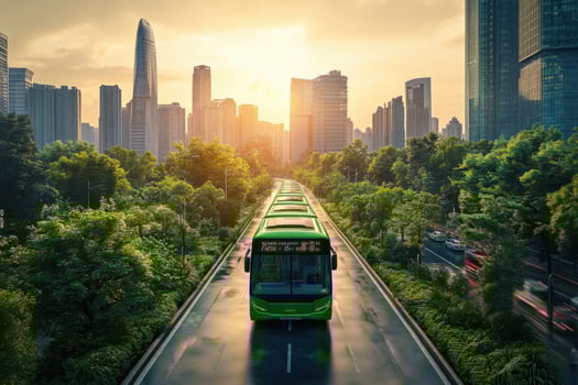 A green bus traveling down a road in front of a city photo