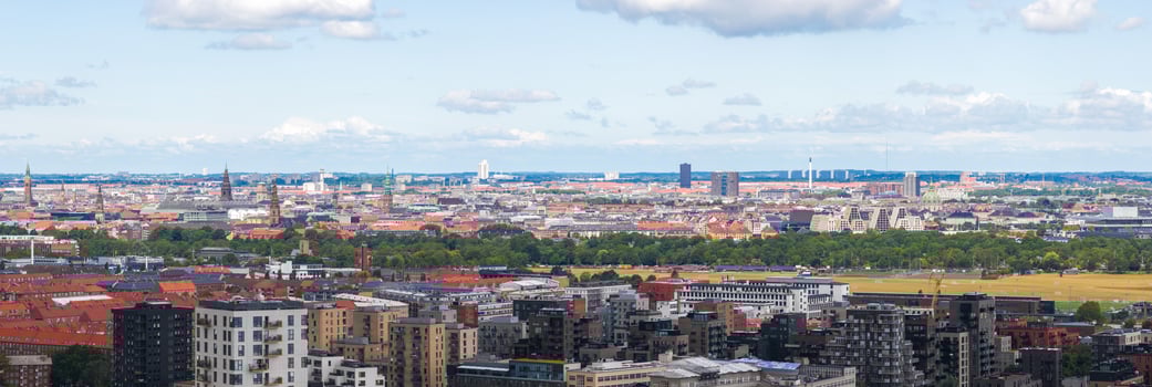 Aerial view of Copenhagen, Denmark, showing historic spires, red roofed buildings, Amager Bakke waste to energy plant, and a large green park. photo