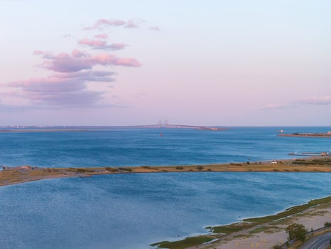 Serene aerial view of Oresund Bridge near Copenhagen, Denmark, during sunset. Calm waters, green land, and soft pink and blue skies are visible. photo