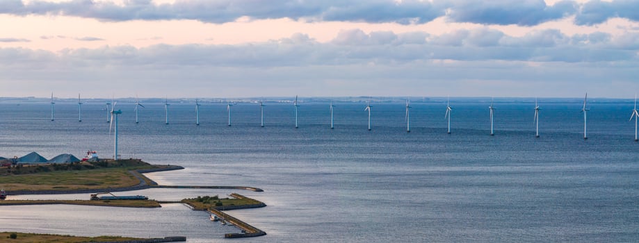 Aerial view of a coastal area near Copenhagen, Denmark, featuring an offshore wind farm, a small peninsula with industrial structures, and calm waters. photo