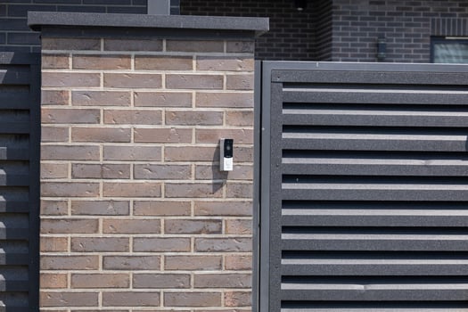 Modern intercom system mounted on a brick wall next to a slatted fence creates a welcoming home entrance during the day photo
