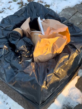 Black trash bag overflowing with recyclable and non-recyclable waste in a snowy outdoor location on a chilly afternoon photo