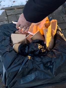 Someone is throwing away litter, including coffee cups and paper bags, into a black trash bag on a cold afternoon photo