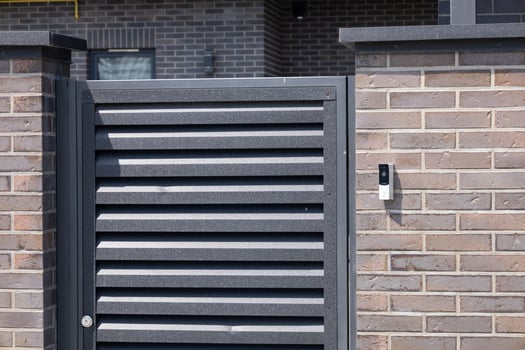 Sleek black slatted door stands closed at an urban home entrance, featuring a security device mounted nearby on the wall photo