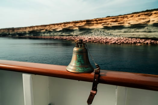 Antique ship bell on yacht rail with coastal cliffs photo