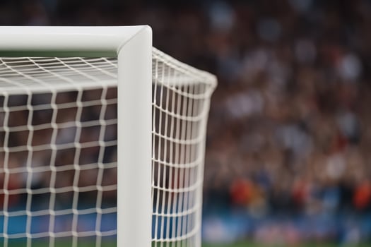 Soccer field goalpost with white netting in football stadium during match with blurred crowd in background creating exciting atmosphere photo