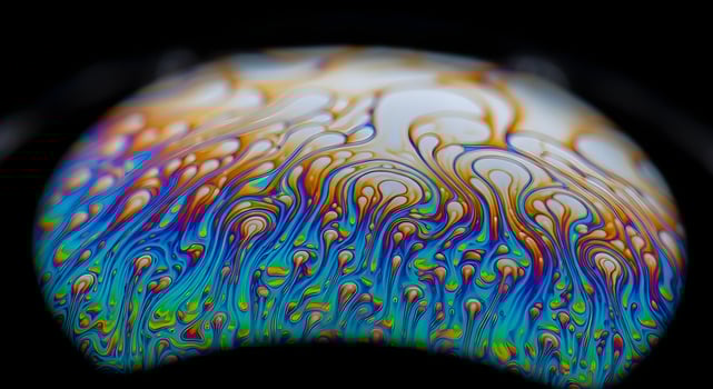Macro abstract photo of soap bubble surface showing vivid swirling colors and crisp ultra-sharp texture with clean black background