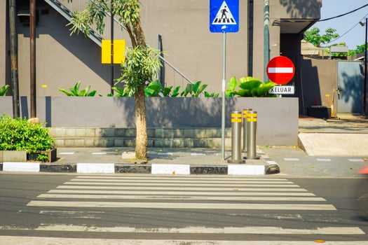 A city street corner with a zebra cross, traffic signs, and pedestrian bollards on a sunny day. photo