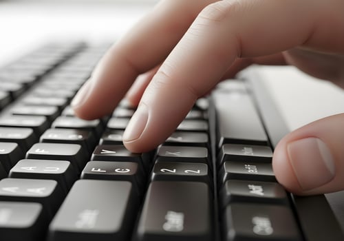 Side angle photo of desktop keyboard with cropped view of one hand typing, crisp detail on keys and fingers under office lighting