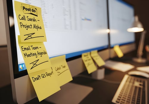 Close-up of sticky notes with handwritten to-do lists attached to computer monitor in clean office workspace, sharp details and no blur photo