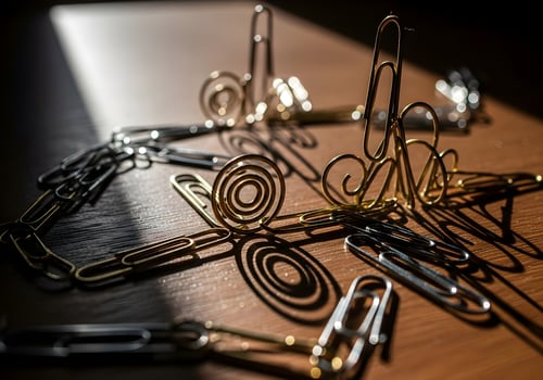 Macro close-up of creatively arranged paperclip chain on office desk with dramatic shadows and strong natural light, no people photo