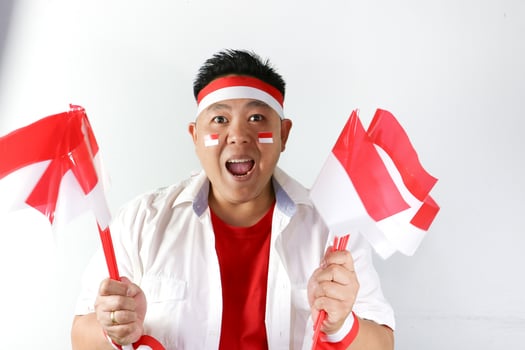 Screaming out loud Indonesian guy holding red white flags and winning gesture photo
