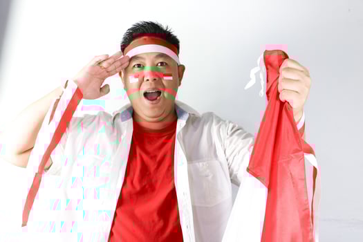 Excited young Indonesian man holding a red and white indonesian flag with salute gesture photo