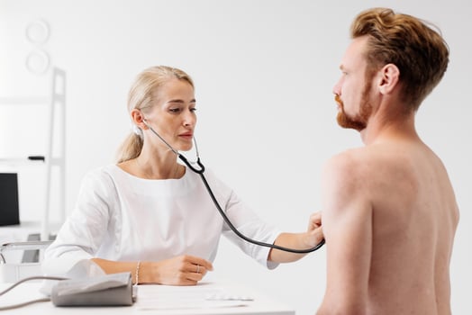 Female doctor in white coat using stethoscope to examine male patient in modern clinic, showcasing attentive care and professional medical environment with medical equipment photo