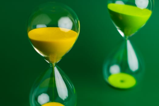 Yellow hourglass close up photo on green background. Concept of quality work and time management.