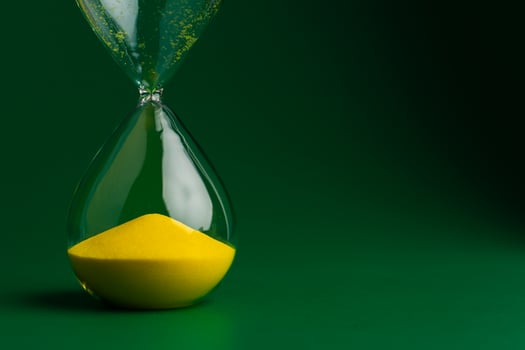 Yellow hourglass close up photo on green background. Concept of quality work and time