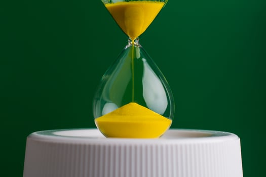 Yellow hourglass close up photo on green background. Concept of quality work and time management