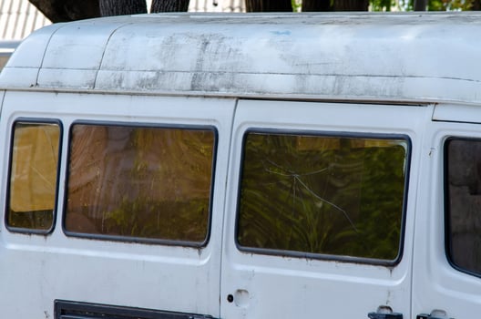 A white van with a dirty windshield and a black door. The van is parked outside. The windows are dirty and the van is in a state of disrepair photo