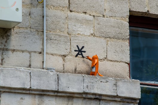 A cat is painting a wall with a spray can. The cat is orange and is standing on a ledge photo