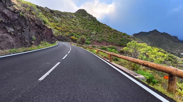 A beautifully winding road winds its way through vibrant greenery and rocky hills, framed by a clear blue sky above photo