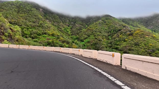 A beautiful winding road gracefully curves through vibrant greenery and rocky hills beneath an enchanting cloudy sky photo