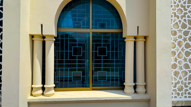 Intricate blue glass window with geometric pattern stands between symmetrical columns outside building photo