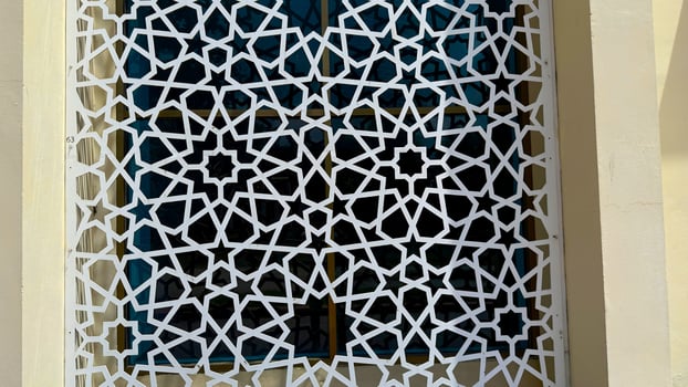 White geometric star pattern creates a decorative lattice screen over a window on a wall photo