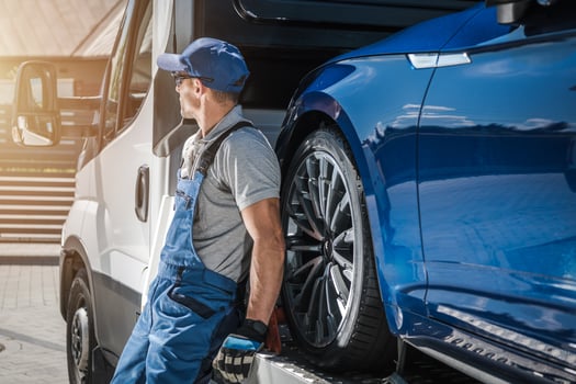 Vehicle Technician Working by a Truck Transporting a Luxury Car at Sunset photo