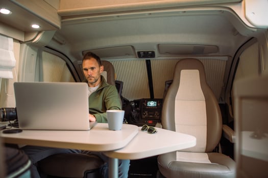Caucasian Man Working on Laptop Inside Modern Camper Van During Daytime Travel photo