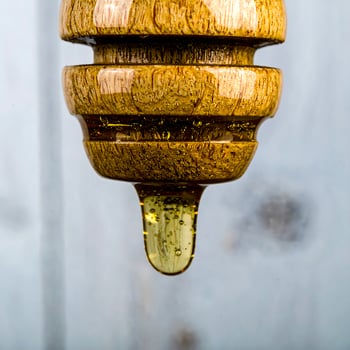 Rich golden honey slowly drips from a rustic wooden dipper, capturing pure sweetness photo