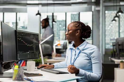 Day trader working for hedge fund company buys and sells stocks to capitalize on market fluctuations. African american woman in prop firm office uses price charts to identify fast profit opportunities photo