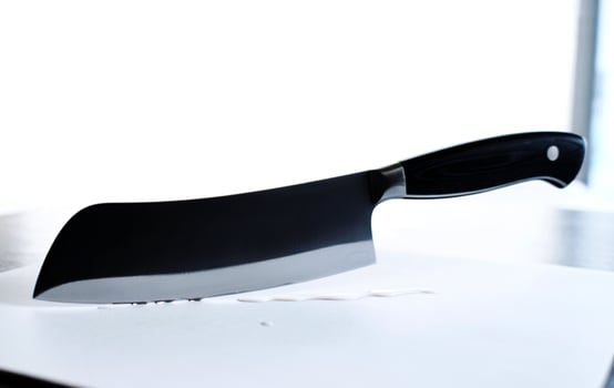 Sharp cleaver knife with black handle resting on a white surface photo