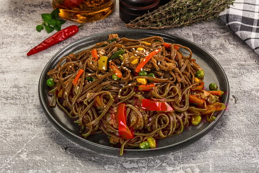 Noodles with vegetables and chili sauce on a black plate photo