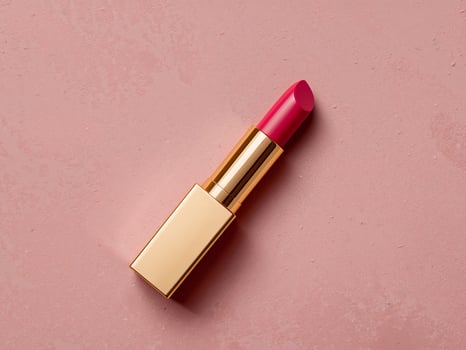 Elegant Gold Lipstick with a Vibrant Pink Hue on a Textured Pink Surface. photo