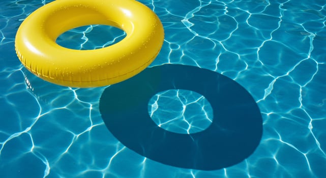 Bright Yellow Inflatable Ring Floating on Shimmering Blue Pool Water Casting a Dark Shadow photo