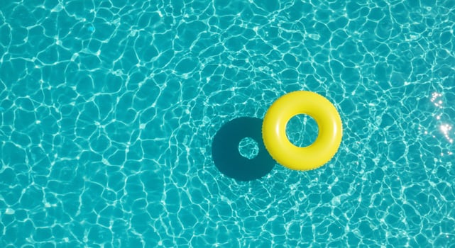 Top-down view of a vibrant yellow inflatable ring floating in a turquoise swimming pool with sun-dappled water photo