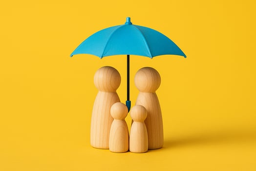Close up of wooden family figurines under a blue umbrella on yellow background representing family insurance and safety photo