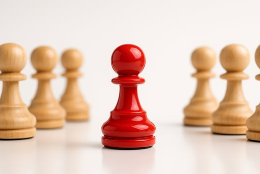 A red figurine standing apart from a group of natural figurines symbolizing isolation, authority, or alienation. photo