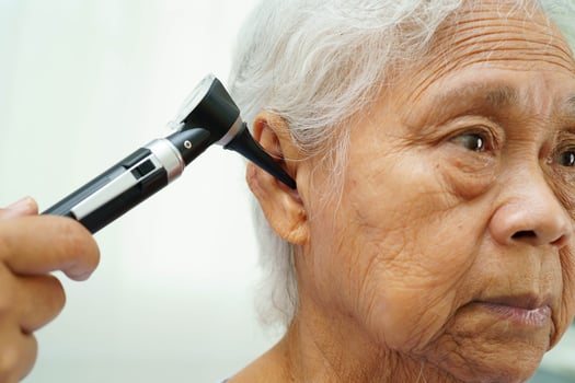 Otolaryngologist or ENT physician doctor examining senior patient ear with otoscope, hearing loss prob photo