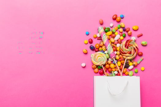 shopping paper gift bag corner full of assorted traditional candies falling out on colored background photo